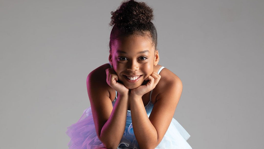 Ballet dancer wearing a purple tutu smiling at the camera 