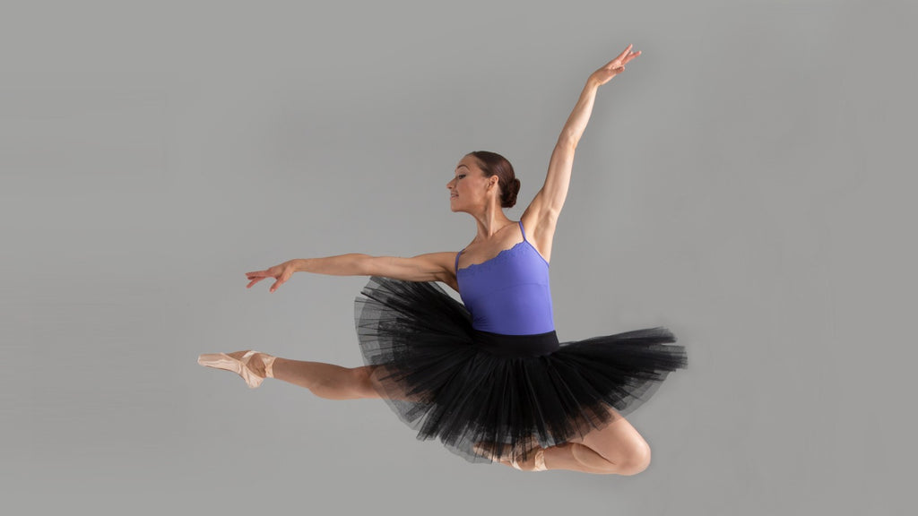 A ballet dancer leaping through the air wearing a BLOCH lilac camisole leotard with black tutu and pointe shoes